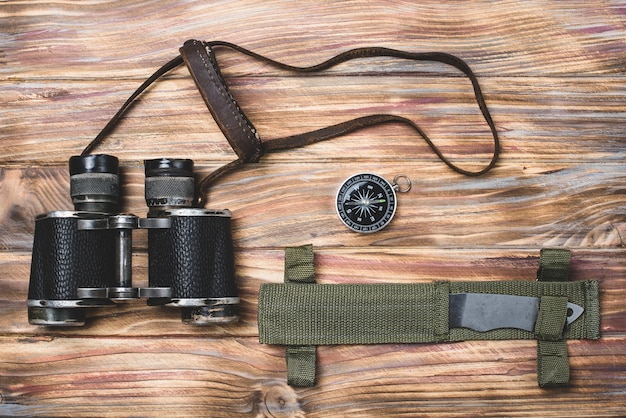 Free photo top view of knife, compass and binoculars on wooden surface