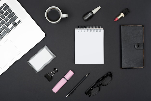 Top view of laptop with coffee cup; lipstick; nail varnish and office stuff against black background