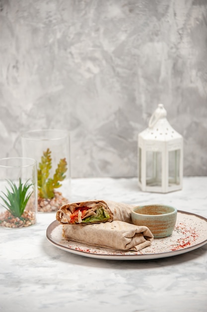 Top view of lavash wrap and yogurt in a small bowl on a plate and toy house on stained white surface