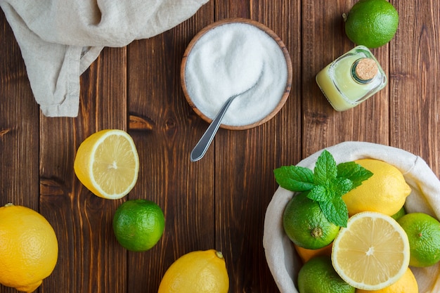 Top view lemons in basket with white cloth, bowl of salt, half of lemon on wooden surface. vertical