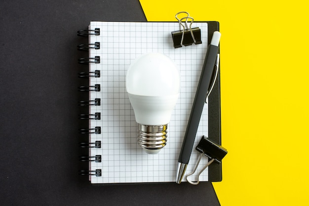 Top view of lightbulb spiral notebook on book and pens on black yellow background with free space