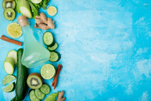 Top view of lime juice with lemon kiwi lime cinnamon ginger and others on left side on blue background with copy space