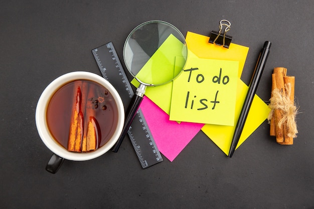 Free photo top view to do list written on yellow sticky note colorful sticky notes lupa pen cinnamon sticks ruler cup of tea