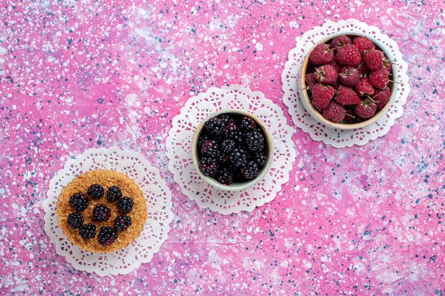 Top view of little blackberry cake with raspberries and fresh blackberries on light pink surface