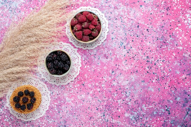 Top view of little blackberry cake with raspberries and fresh blackberries on the light pink surface