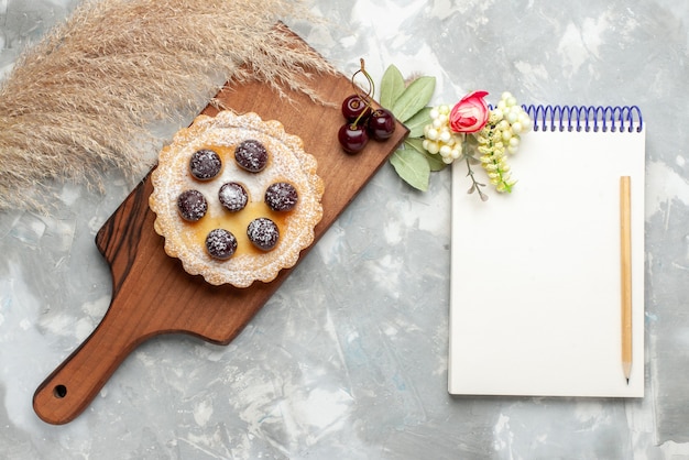 Top view of little cake with sugar powder fruits cream and notepad on light, cake cream fruit sweet tea