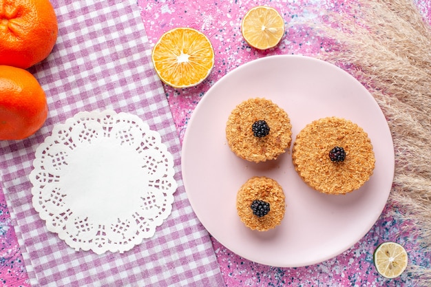 Top view of little cakes with berries inside plate on pink surface