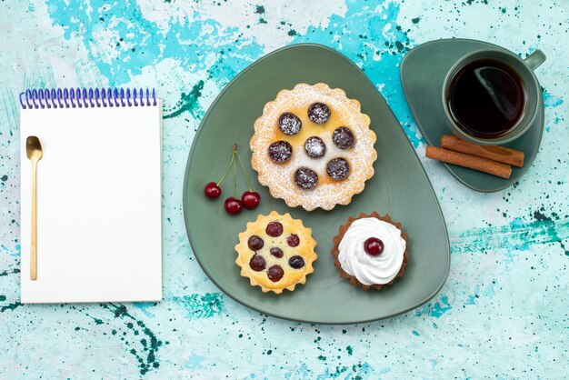 Free Photo top view little cakes with fruits inside plate along with tea and notepad on the light-blue table cake bake sweet sugar tea color