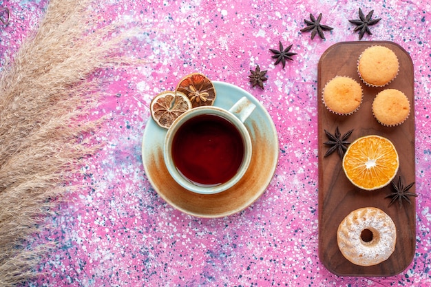 Free photo top view of little cakes with orange slice and cup of tea on light-pink surface