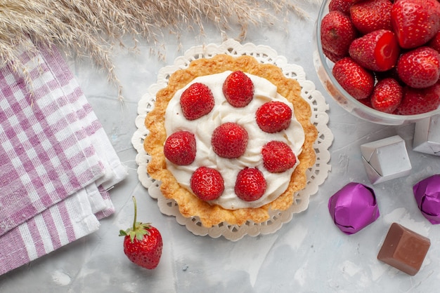 Free photo top view little creamy cake with fresh red strawberries and chocolate candies on the white-light desk cake fruit berry biscuit cream