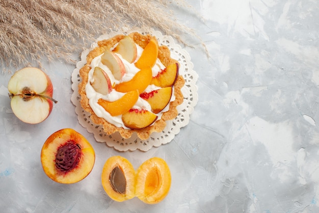 Top view little creamy cake with sliced fruits and white cream along with fresh apricots and peaches on white light desk fruits biscuit cookie