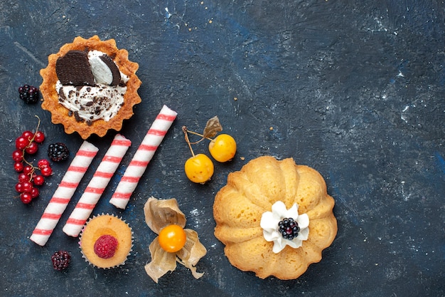 Free photo top view little delicious cake along with cookie and pink stick candies fruits on the dark desk biscuit cake sweet fruit