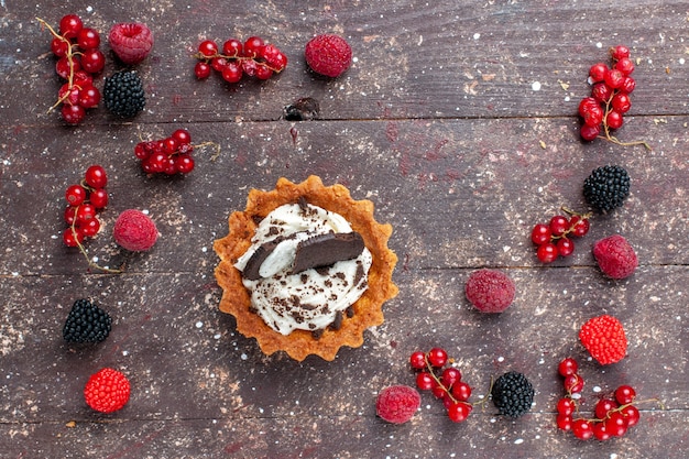 Free photo top view little delicious cake along with different colored berries spread all over the brown floor berry fruit color bake biscuit