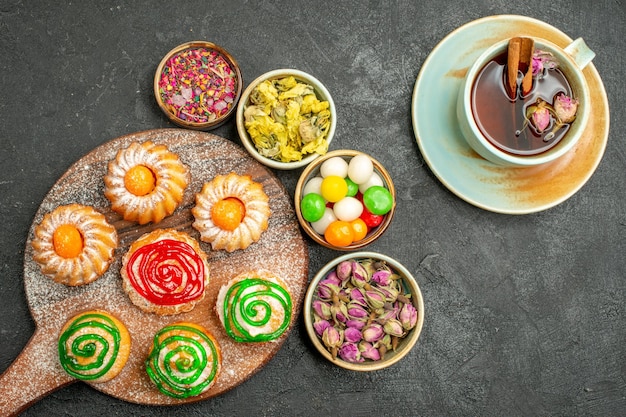 Free Photo top view of little delicious cakes with candies tea and flowers on black