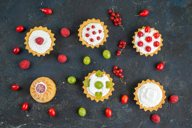 Top view little delicious cakes with cream and fresh fruits on the dark desk fruit 