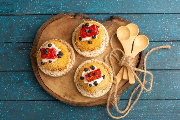 Free Photo top view of little delicious cakes with fruits on the brown wooden board and blue surface