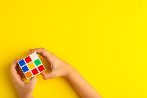 Free Photo top view little kid playing with rubics cube on the yellow surface