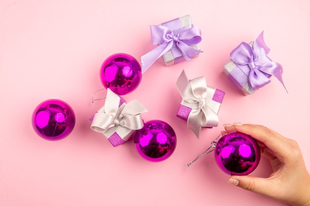 Top view of little presents with xmas tree toys on pink surface