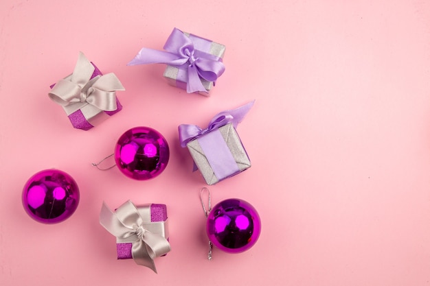 Top view of little presents with xmas tree toys on pink surface