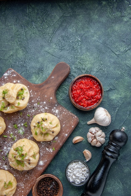 Free Photo top view little raw dumplings with tomato sauce on the dark blue surface dinner meat dough dish cake meal cooking cuisine