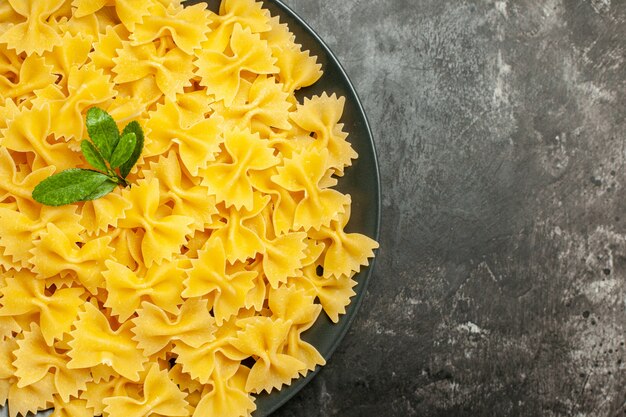 Top view little raw pasta inside plate on dark-grey background