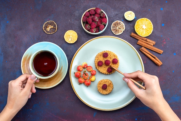 Free photo top view of little round cake with fresh raspberries inside plate with fruits cinnamon tea on dark surface