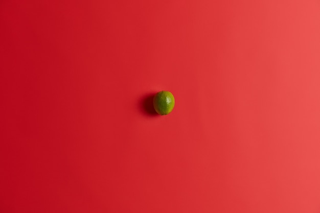 Free photo top view of little sour green lime lying on red vibrant surface, contains much vitamins. fresh juicy citrus fruit for nutrition. ingredient for making mojito or lemonade. healthy food concept.