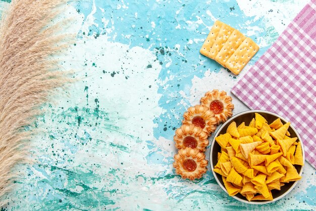 Top view little spicy chips inside plate with crackers and cookies on light blue background chips snack color crisp calorie