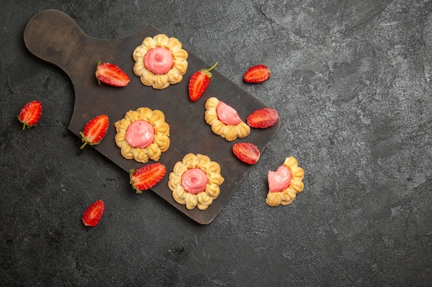 Top view of little sugar cookies with strawberry cream on grey surface