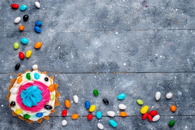 Top view little yummy cake with cream and different colorful candies all over the light background candy sweet color cake photo