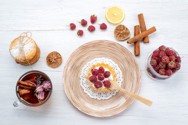 Top view little yummy cake with cream and raspberries along with sandwich cookies cinnamon tea on the light-white table fruit berry cake biscuit sweet