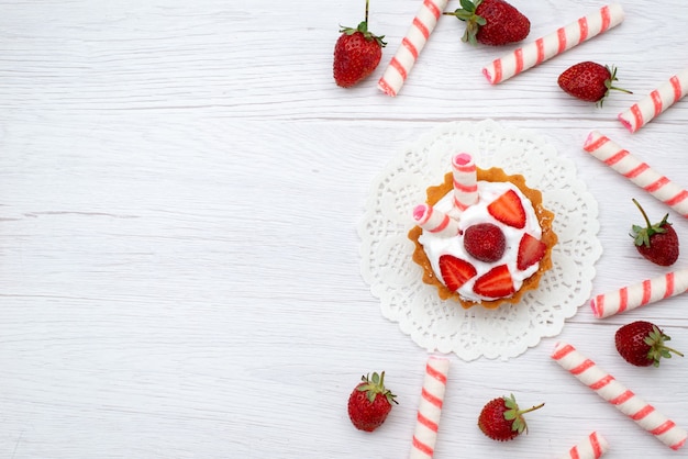 Top view little yummy cake with cream and sliced strawberries stick candies on the white background cake berry sweet sugar bake