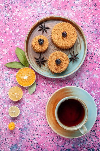 Top view of little yummy cakes sweet and delicious inside plate with tea on the pink surface