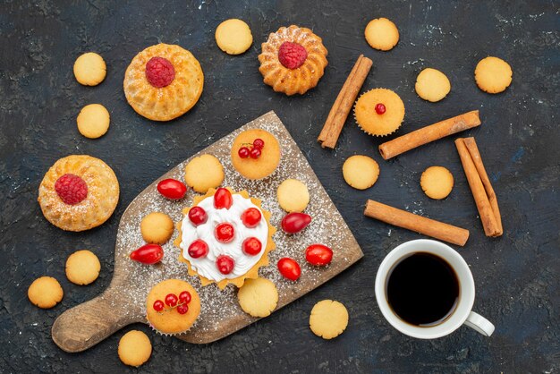 Top view little yummy cakes with cream cinnamon coffee and fresh fruits on the dark desk sweet biscuit cake dessert fruit berry