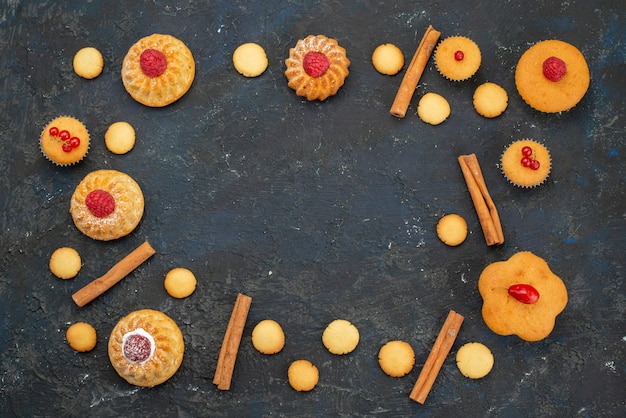 Top view little yummy cakes with cream cookies cinnamon on the dark desk sweet biscuit cake dessert fruit berry