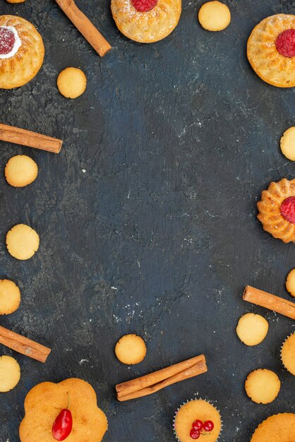 Top view little yummy cakes with cream cookies cinnamon on the dark desk sweet biscuit cake dessert fruits