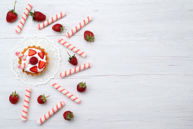 Free photo top view little yummy cakes with cream and sliced strawberries candies on the white background cake berry sweet bake