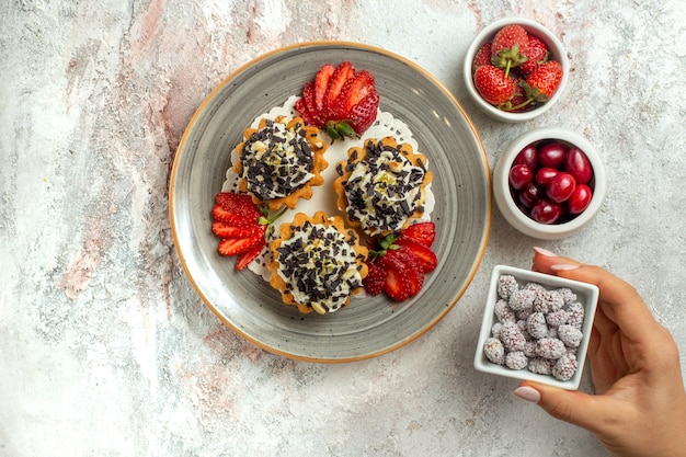 Free Photo top view little yummy cakes with strawberries and candies on white surface birthday celebration sweet biscuit cake