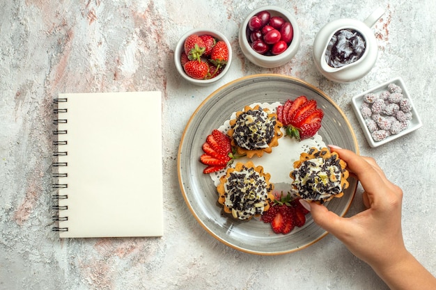 Free photo top view little yummy cakes with strawberries and candies on white surface celebration tea sweet biscuit sugar cake cream