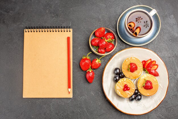 Top view little yummy pancakes with fruits and cup of tea on grey floor pie cake fruit