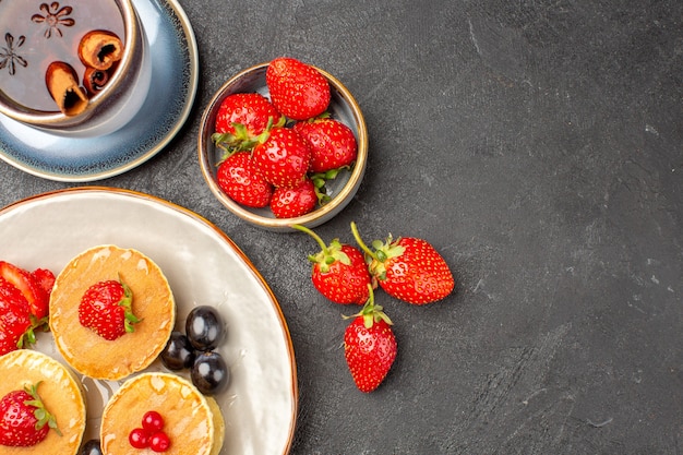 Top view little yummy pancakes with fruits and cup of tea on a grey surface pie cake fruit