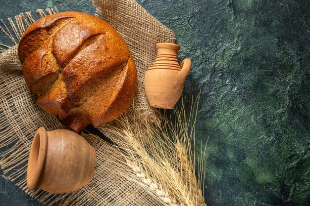 Top view of a loaf of dietary black bread on brown towel and potteries on the right side on dark colors background