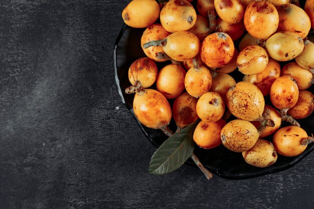 Top view loquats in bowl with leaves on dark textured background. horizontal