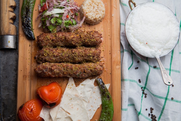 Free Photo top view lula kabab with fried vegetables and chopped onion and ayran and knife in cutting board