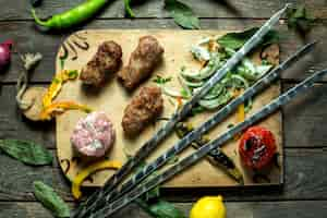 Free photo top view of lula kebab with onion herbs grilled vegetables and skewers on a wooden board