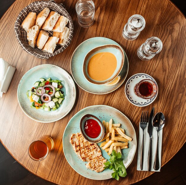 Top view of lunch setup with grilled chicken dish lentil soup bread and greek salad