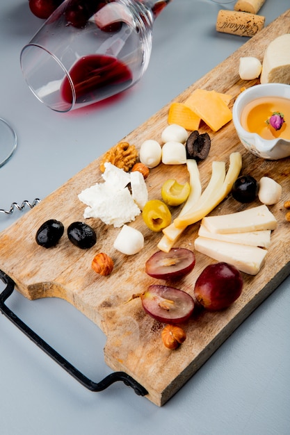 Free Photo top view of lying glass of red wine with different kinds of cheese grape olive nuts butter on cutting board and cork on white 1