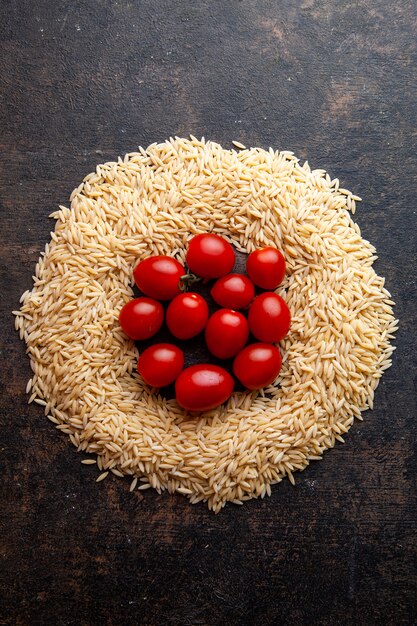 Top view macaroni in a circle form with tomatoes on them on dark textured background. vertical