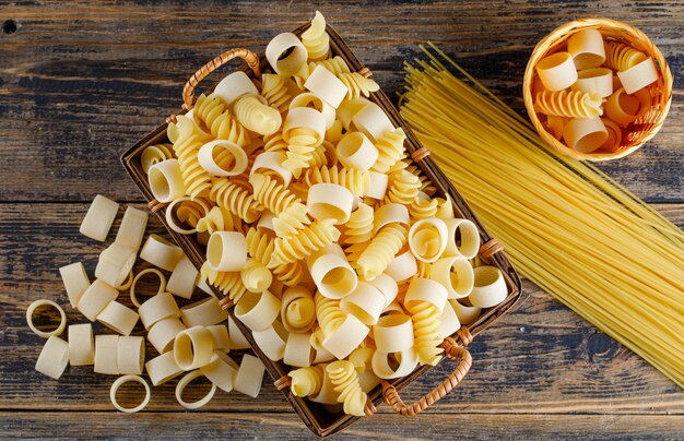 Top view macaroni pasta in tray and small bucket with spaghetti on wooden background. horizontal