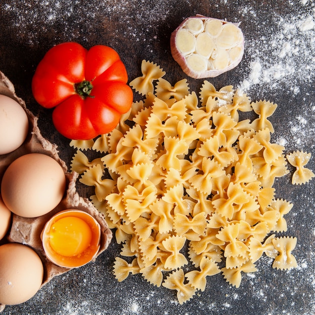 Free Photo top view macaroni with eggs, tomato and garlic on dark textured background.